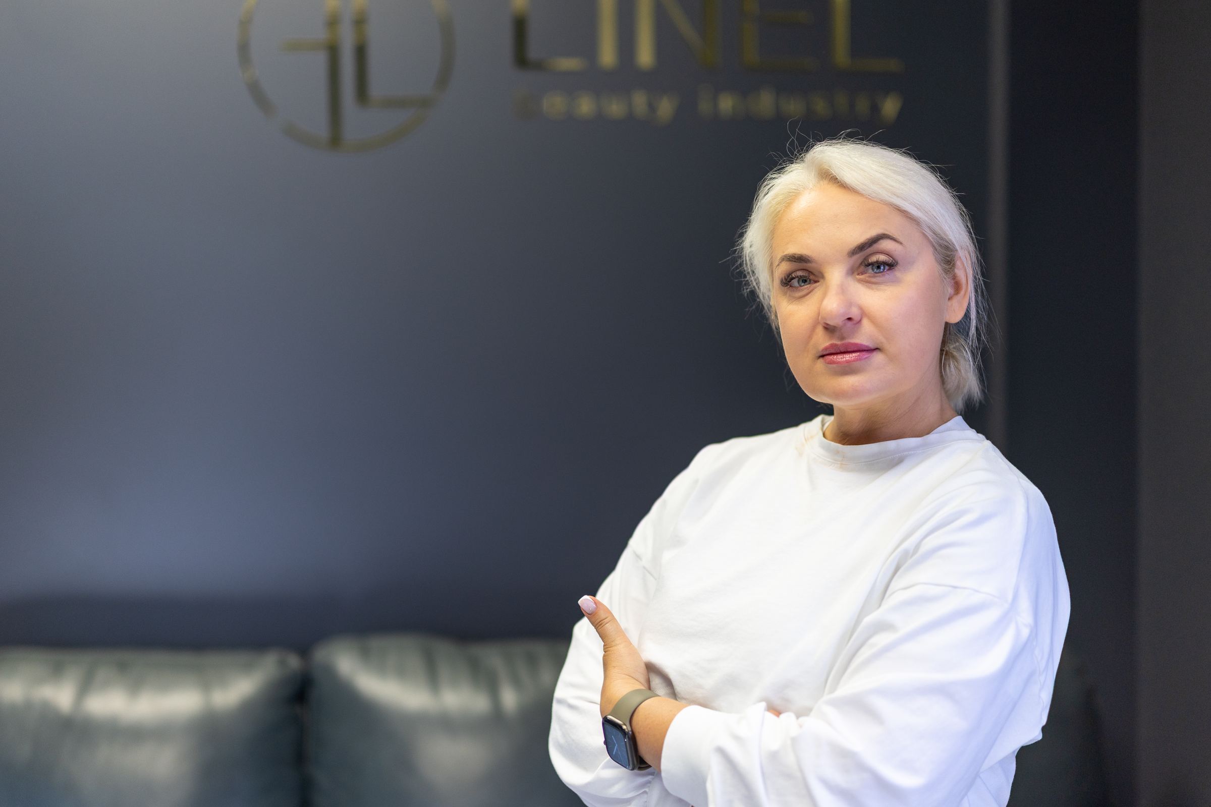 Olena Burykina, arms crossed, in the LINEL reception area under the LINEL sign